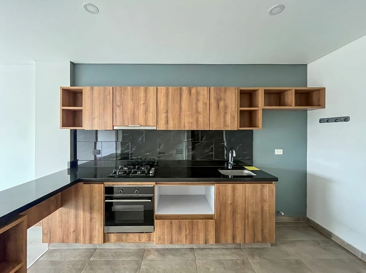Cocina en L con mesón en granito negro, estufa a gas, horno y muebles en aglomerado laminado MDP